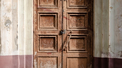 Abandoned old door with the lock. Rust on the metal lock. Peeling brown paint on the old door.