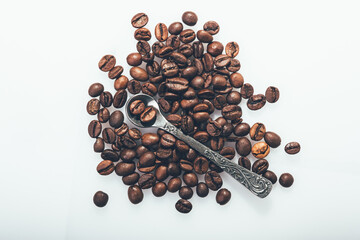 A pile of coffee beans with a coffee spoon on a light background.