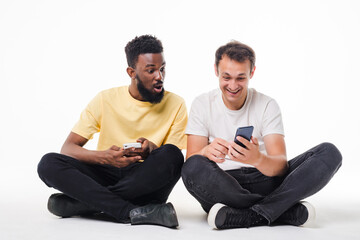 Portrait of a two young men holding mobile phones and looking at each other isolated over white background