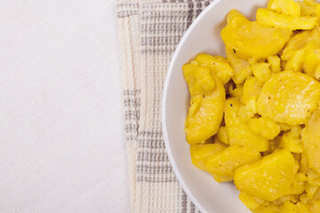 Stewed potato with spices in bowl on checkered napkin.