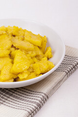 Stewed potato with spices in bowl on checkered napkin.