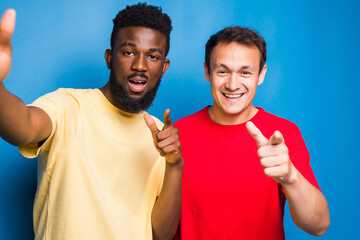 Two mixed race men pointed on camera take selfie isolated on blue background