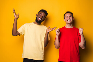 Portrait of a two happy young men win gesture after soccer isolated over yellow background
