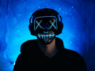 Portrait of a guy with headphones and a glowing Halloween mask . Autumn party