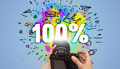 Close-up of a hand holding digital camera with abstract drawing and 100% inscription