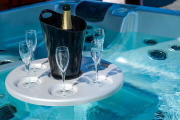 A bottle of champagne in a black ice bucket and glasses on the table in the jacuzzi. Soft focus background. Close-up