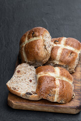 Easter wholemeal hot cross buns on wooden board on black stone background