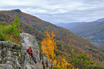 A hiker woman holds her camera and looks down the valley from the top of Seneca Rocks hike in West...