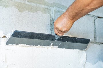 Man apply plaster to the wall using a spatula. Renovation and construction concept