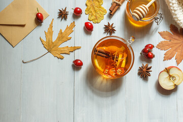 Autumn flatlay with fragrant hot tea, dry leaves, an envelope and a knitted blanket. On a light wooden background with space