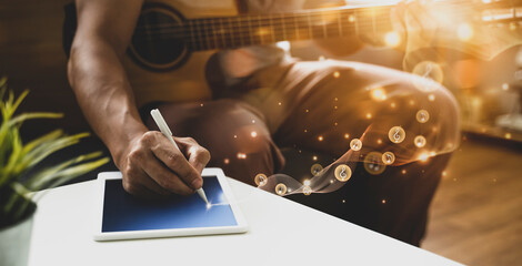Musician artist guitarist playing on musical instrument guitar writing songs using smart tablet...