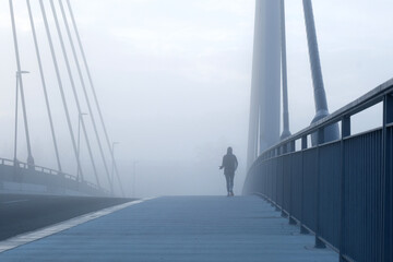 Joggerin läuft bei Nebel über eine Brücke 