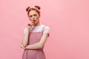 Red-haired girl with buns looks at camera thoughtfully. Portrait of woman in pink jumpsuit and white top