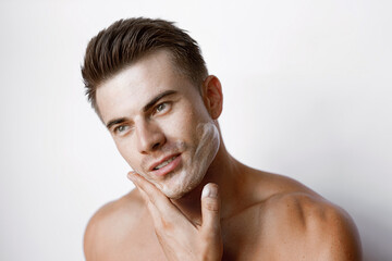 Fototapeta na wymiar Muscular sexy model sports young man on white background. Portrait of beautiful smiling healthy guy applying foam for washing on his face. Facial skincare routine.