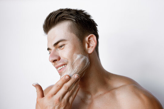 Muscular Sexy Model Sports Young Man On White Background. Portrait Of Beautiful Smiling Healthy Guy Applying Foam For Washing On His Face. Facial Skincare Routine.