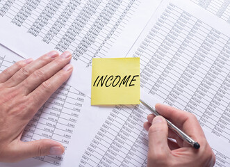 INCOME word on yellow note paper on financial documents with male hands, flatly, top view