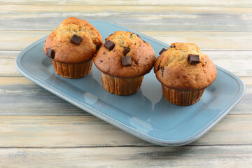 Three banana chocolate chunk muffins in paper cups on blue serving platter