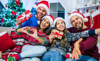 Group of beautiful best friends in Santa hats with gifts in hands are posing and having fun on Christmas tree background at home party