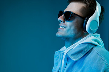 Obraz premium Portrait of man in headphones listening music. Blue background. Guy in denim jacket expresses happiness.