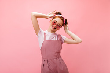 Naughty girl in sunglasses, wearing white top and pink jumpsuit with smile touches her buns