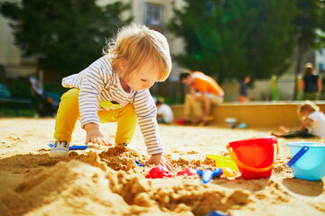 Adorable little girl on playground in sandpit - obrazy, fototapety, plakaty