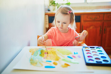 Girl drawing rainbow with colorful aquarelle paints