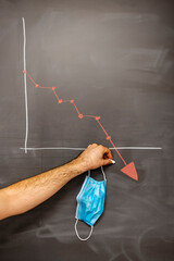 person holding face mask and pointing red descending graph on blackboard