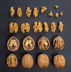 Creative composition walnuts on black slate background. Whole and opened nuts, broken, cracked and shelled kernel autumn food set.