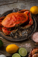 Metal dark round plate with big crab served with ice cube, lime, bowl with sea salt and seashells....