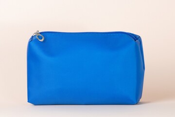 A blue makeup bag with a zipper stands on a pink background