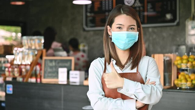 Portrait of Asian female barista wearing face mask looking at camera working while social distancing