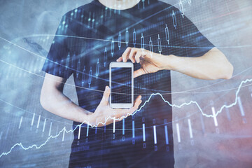 Double exposure of man's hands holding and using a digital device and forex graph drawing. Financial market concept.