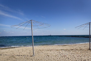 Lonely sandy empty autumn beach with metal umbrellas silhouette and blue sea water horizon at the end of summer season  