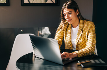Portrait of beautiful businesswoman sitting at table, looking at laptop screen on video call or...