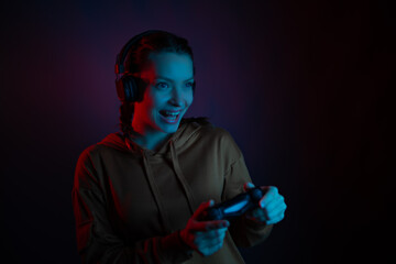 Fototapeta na wymiar A gamer girl with joystick and headphone in dark room playing video game. Emotional smiling face. Excitement. Having fun.