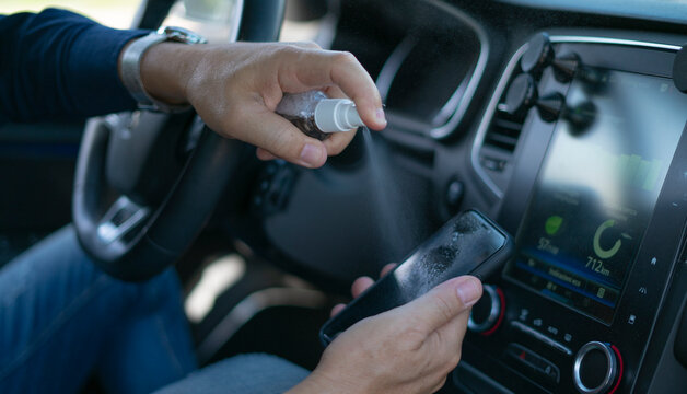 male hand spraying disinfectant spray on your smartphone screen inside the car
