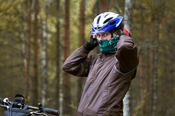 Young man wearing bicycle helmet and face mask to protect himself from coronavirus. Man is riding his bicycle in the autumn forest to guarantee distance. Concept of new normal. Alternative transport