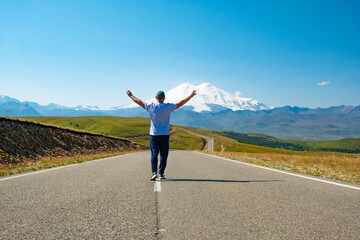 A man walks along the highway against the backdrop of mountains. Freedom and travel concept. Elbrus, Caucasus.