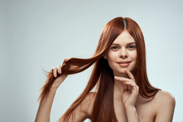 Obraz premium pretty redhead woman holding her hair with hands grooming naked shoulders light background