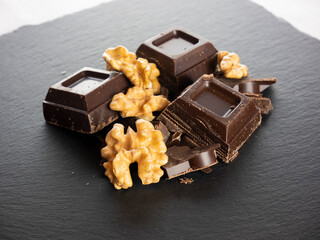 Three squares of dark chocolate with walnut kernel on the black slate background. 