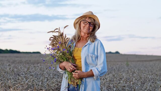 Romantic Image Of Woman With Bouquet On Background Of Sky. She Stands In The Middle Of Wheat Field With Spikelets And Flowers In Her Hands.