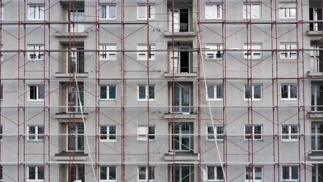 Scaffolding in front of the exterior of a high-rise building plastered with cement plaster - construction of a multistory public housing project. Establishing shot aerial footage.