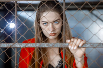 long-haired brunette woman in red behind bars in a cage close-up