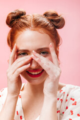 Smiling girl with buns looks at camera. Portrait of lady in blouse with cherries on pink background