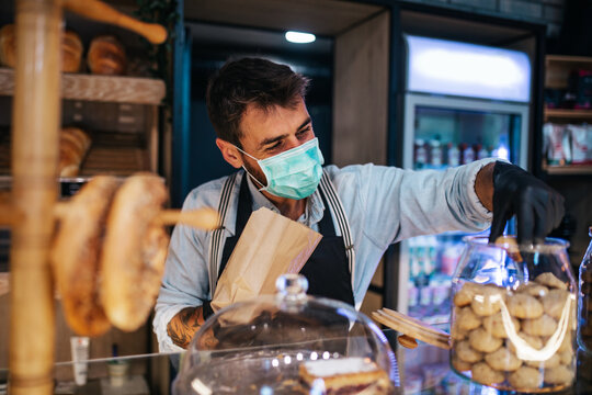 Handsome middle age male worker with protective mask on face working in bakery.