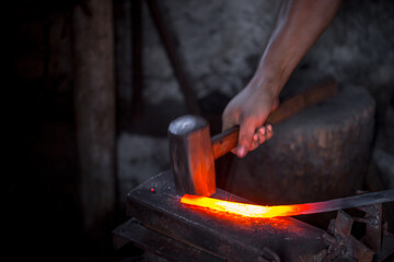 Blacksmith's hands at work. In one hand a hammer, in the other a workpiece of hot metal. Master...