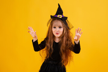 little girl with long red hair smiles in a Halloween witch costume and holds a pumpkin-shaped candy bowl on a yellow background. Halloween for children, space for text