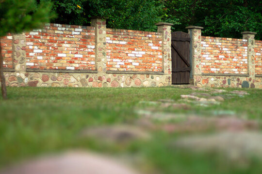 Landscaping. Red brick fence with brown wooden gate in the courtyard of private house. Stone path.