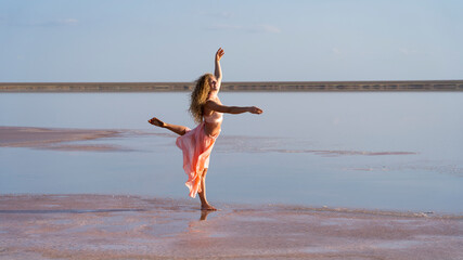 Obraz premium beautiful curly girl balances standing on one leg overlooking the pink sunset