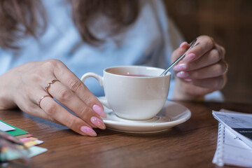 Womans hands on a table with a cup of tea.White cup, business breakfast